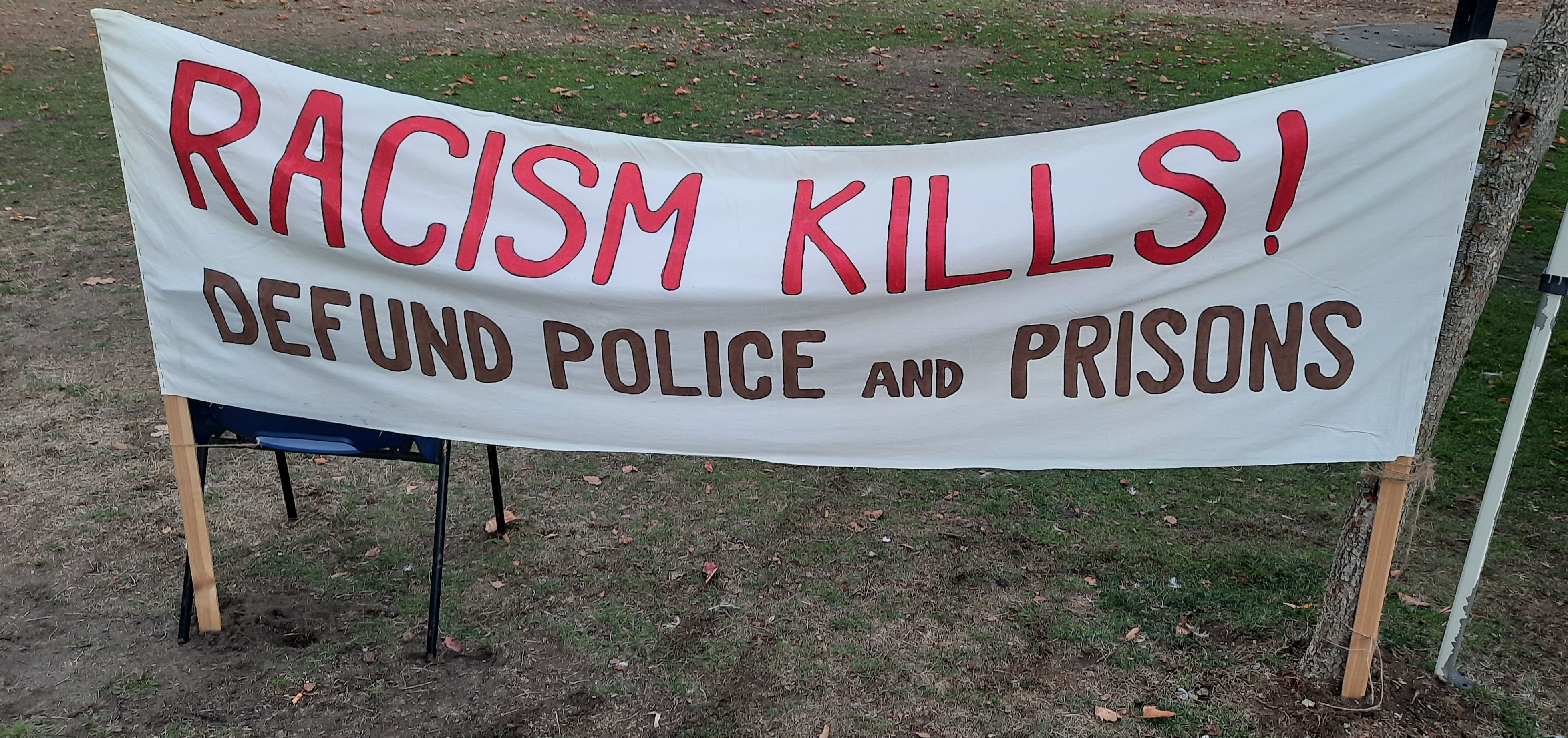 Racism Kills! Defund Police and Prisons. Banner saying, Racism Kills! Defund Police and Prisons