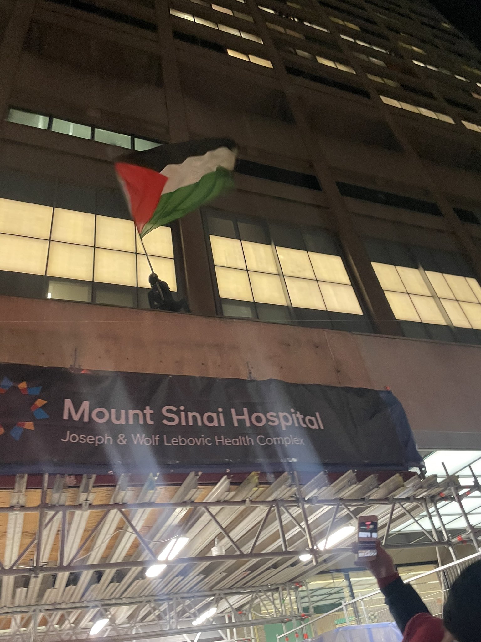 SPIDERMAN4PALESTINE WAVES A PALESTINIAN FLAG ABOVE THE ENTRANCE OF MOUNT SINAI HOSPITAL, ONE OF AT LEAST EIGHT ELEVATED SPOTS THEY CLIMBED TO IN THE COURSE OF THE RALLY ON FEB. 12. PHOTO CREDIT: ANNA LIPPMAN. SPIDERMAN4PALESTINE WAVES A PALESTINIAN FLAG ABOVE THE ENTRANCE OF MOUNT SINAI HOSPITAL, ONE OF AT LEAST EIGHT ELEVATED SPOTS THEY CLIMBED TO IN THE COURSE OF THE RALLY ON FEB. 12. PHOTO CREDIT: ANNA LIPPMAN.