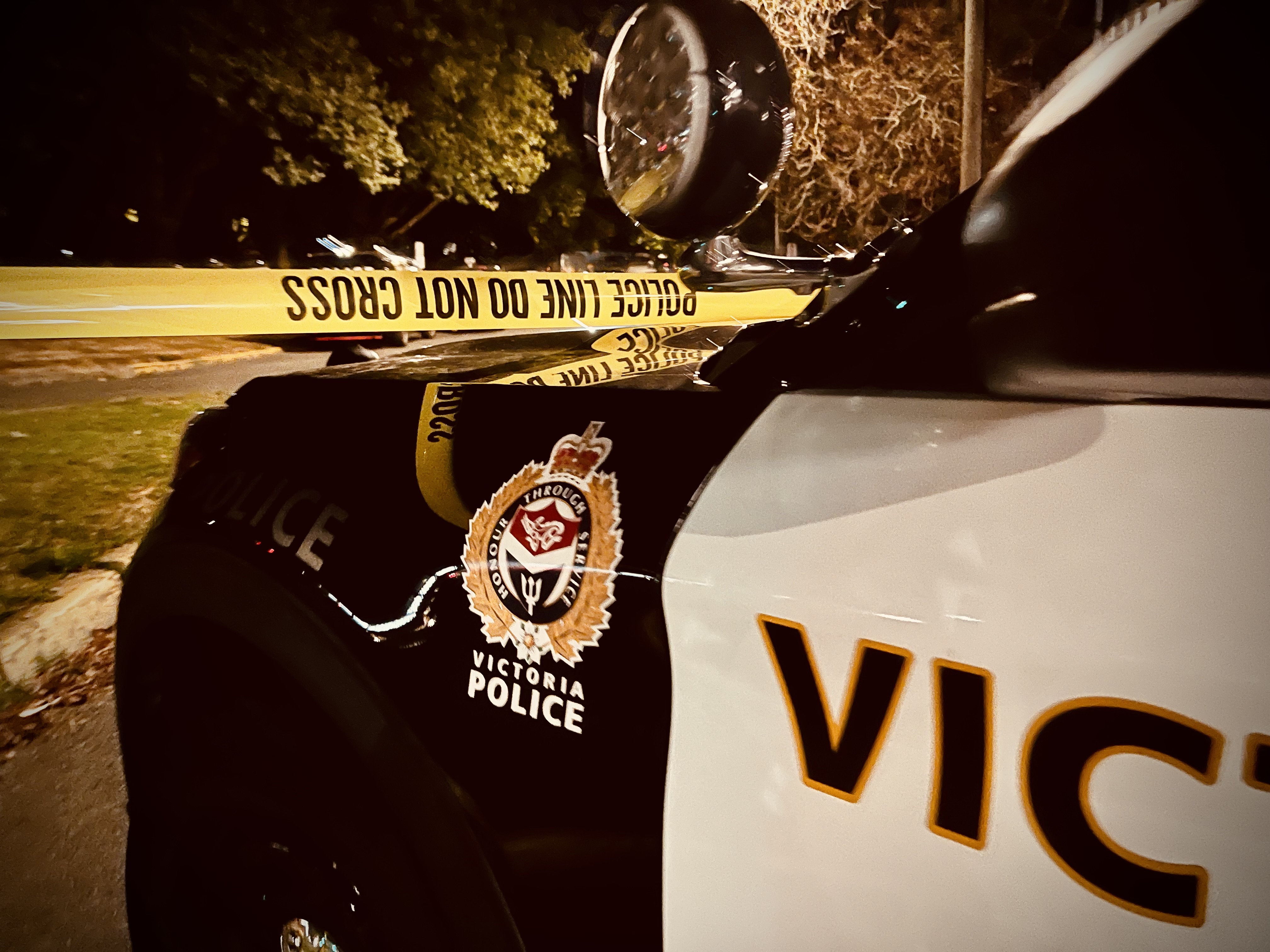 Front of a Victoria Police car at night with caution tape in the background.
