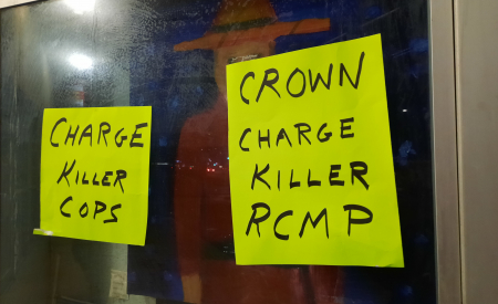 Posters on RCMP window saying charge killer cops and crown charge killer RCMP
