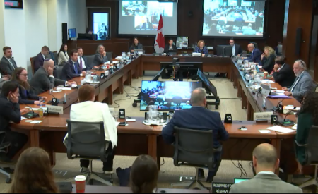 Committee in session at the House of Commons on May 9, 2024. Over a dozen people are sitting facing each other at tables in a rectangular shape.