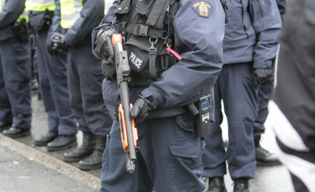 RCMP in riot gear. One standing with shotgun.